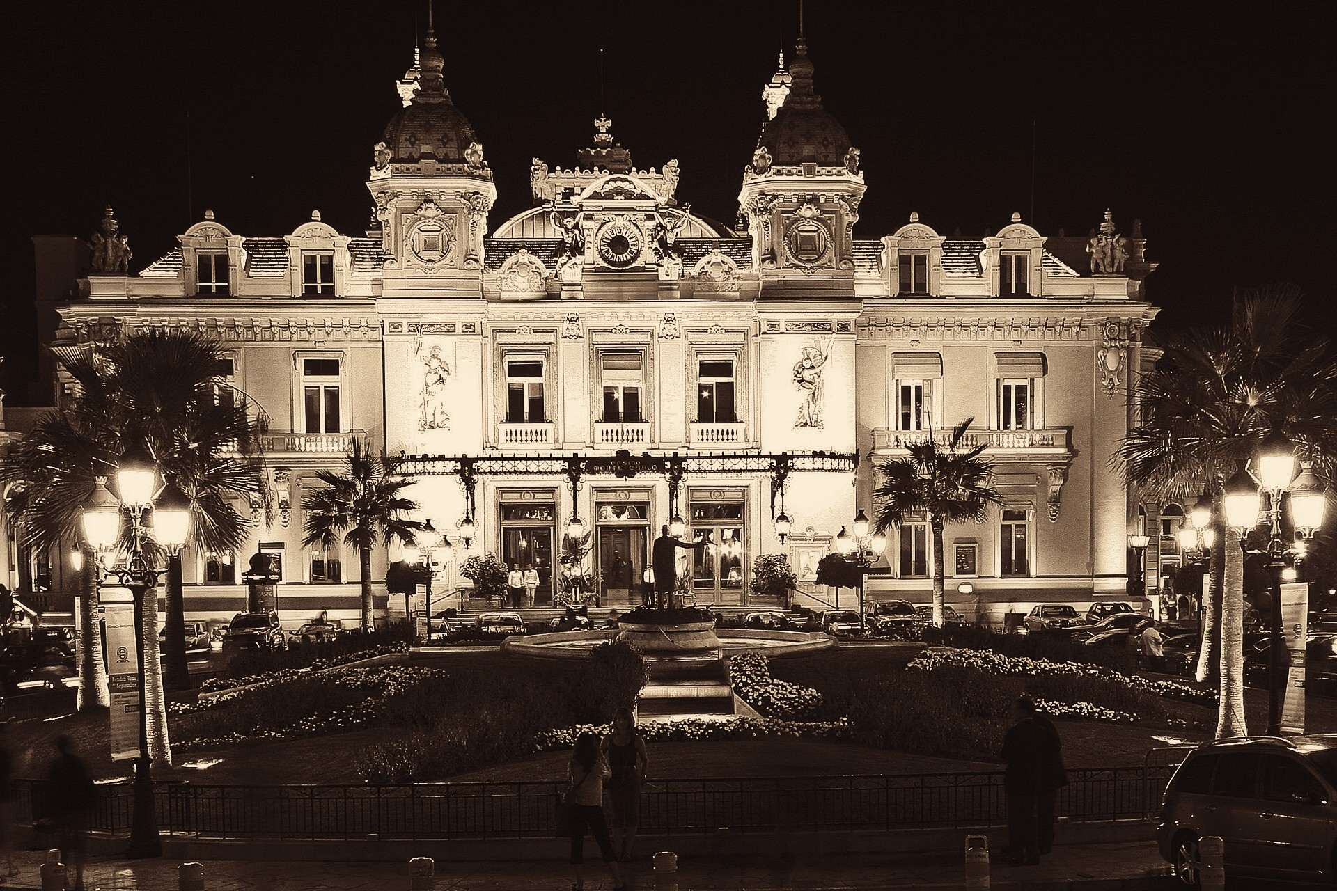 The Casino de Monte-Carlo lit up at night, its twin towers and arched facade behind the palms and fountain of the Place du Casino