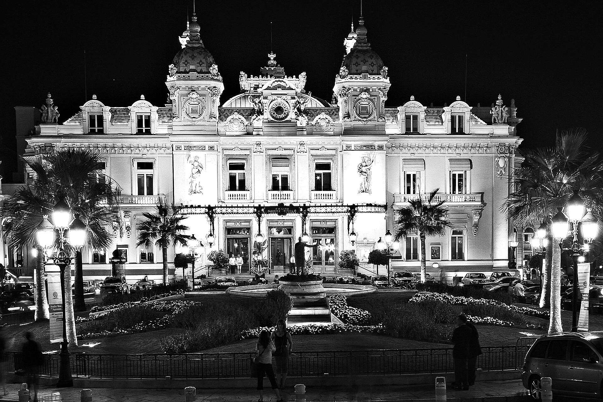 The Casino de Monte-Carlo lit up at night, its twin towers and arched facade behind the palms and fountain of the Place du Casino
